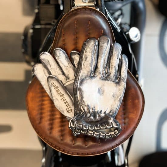 White vintage Memento Mori moto gloves resting on a motorcycle seat.
